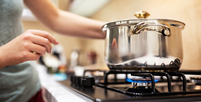 A woman preparing dinner by putting a silver saucepan on a gas oven with a blue flame.