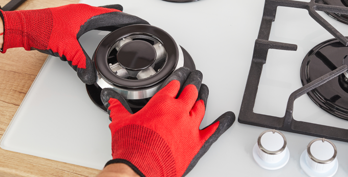 Installing a burner ring on a kitchen gas hob, wearing protective PPE red gloves.