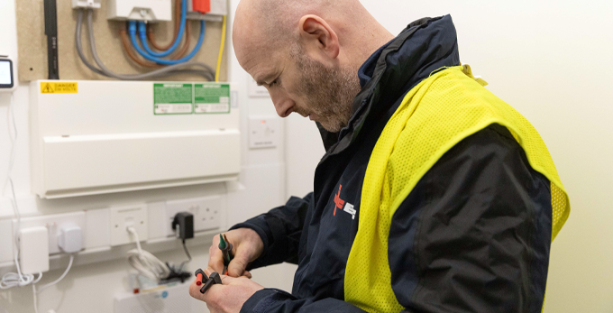 An NICEIC approved contractor, repairing connective wiring on an electric board in a corporate office space.