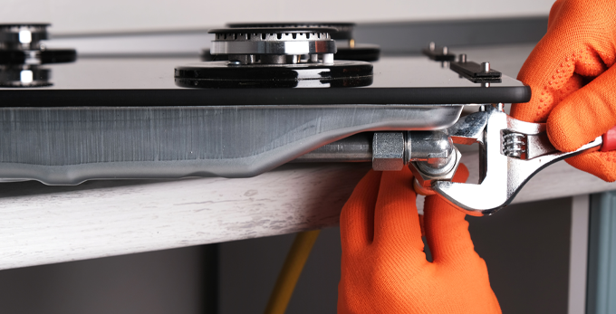 Connecting a gas hose to kitchen hob whilst wearing protective orange gloves and using an adjustable wrench